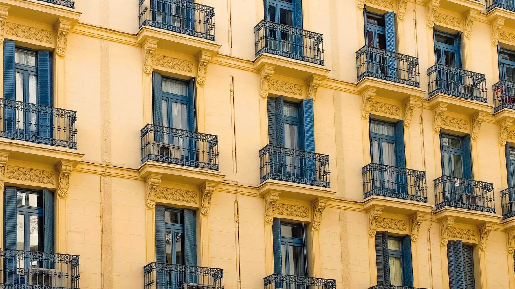 Όψη πολυκατοικίας με ανοιγόμενα παντζούρια περσίδων σε μπλε απόχρωση, πάνω από σιδερένια κάγκελα μπαλκονιών